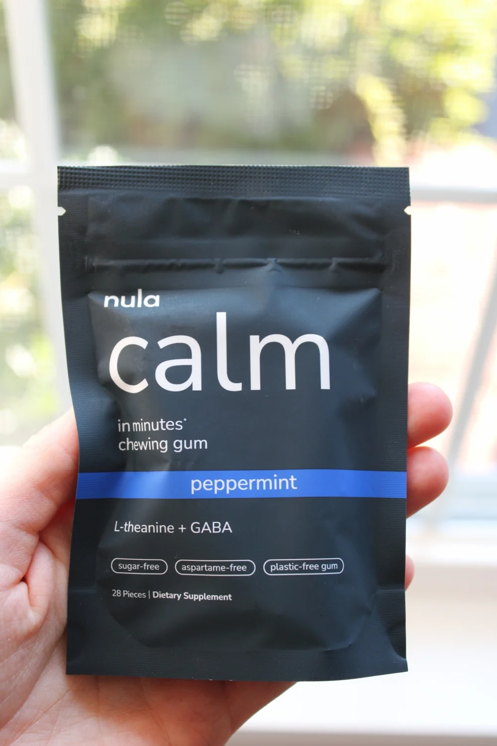 A hand holding a pouch of Nula calm gum by a window